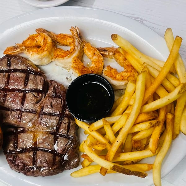 Grilled steak, seasoned shrimp, and golden french fries with a side of dark sauce on a white plate.