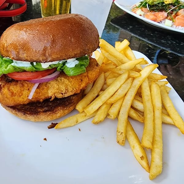 Crispy fish sandwich with lettuce, tomato, onion, and tartar sauce, served with golden french fries.