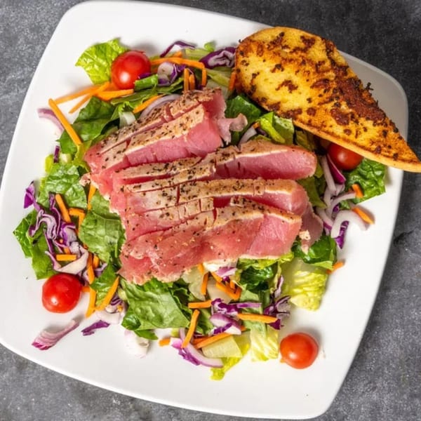 Seared tuna salad with mixed greens, cherry tomatoes, red onion, carrots, and a side of garlic bread.