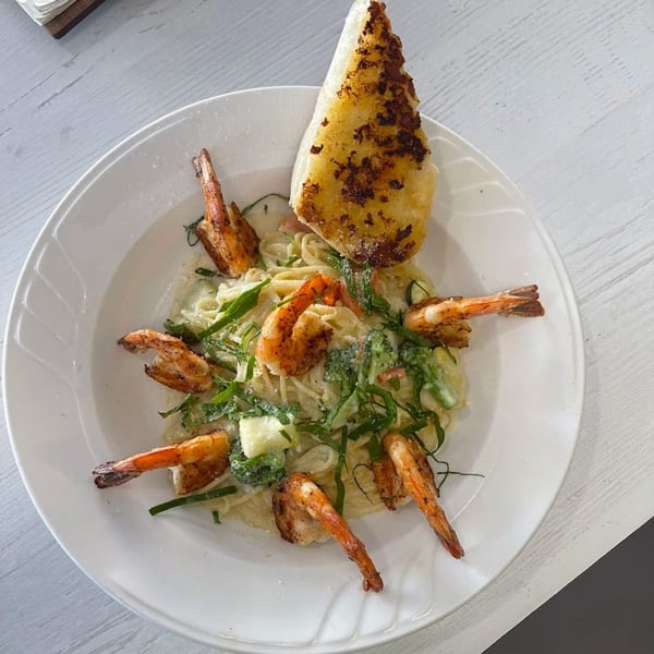 Shrimp pasta with creamy sauce, green vegetables, and a piece of garlic bread on a white plate.