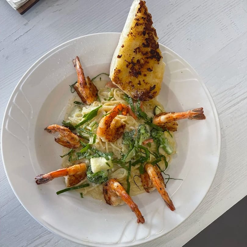 Shrimp pasta with creamy sauce, green vegetables, and a piece of garlic bread on a white plate.