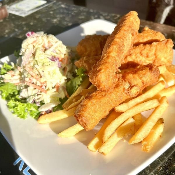 Golden-brown fried fish and french fries with a side of coleslaw and lettuce on a white plate.