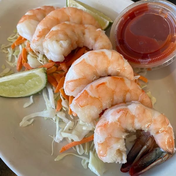 Five large cooked shrimp on a bed of shredded cabbage and carrots with lime and cocktail sauce.